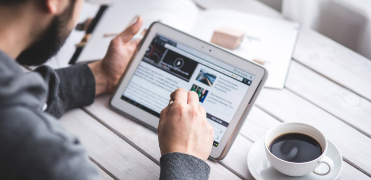 Man reading news on a tablet with a cup of coffee next to him